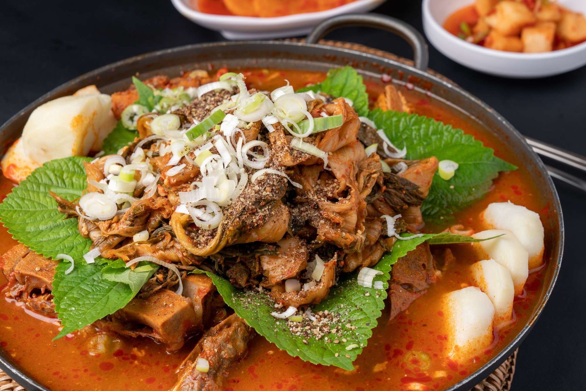A close up of a bowl of soup with meat and vegetables on a table.
