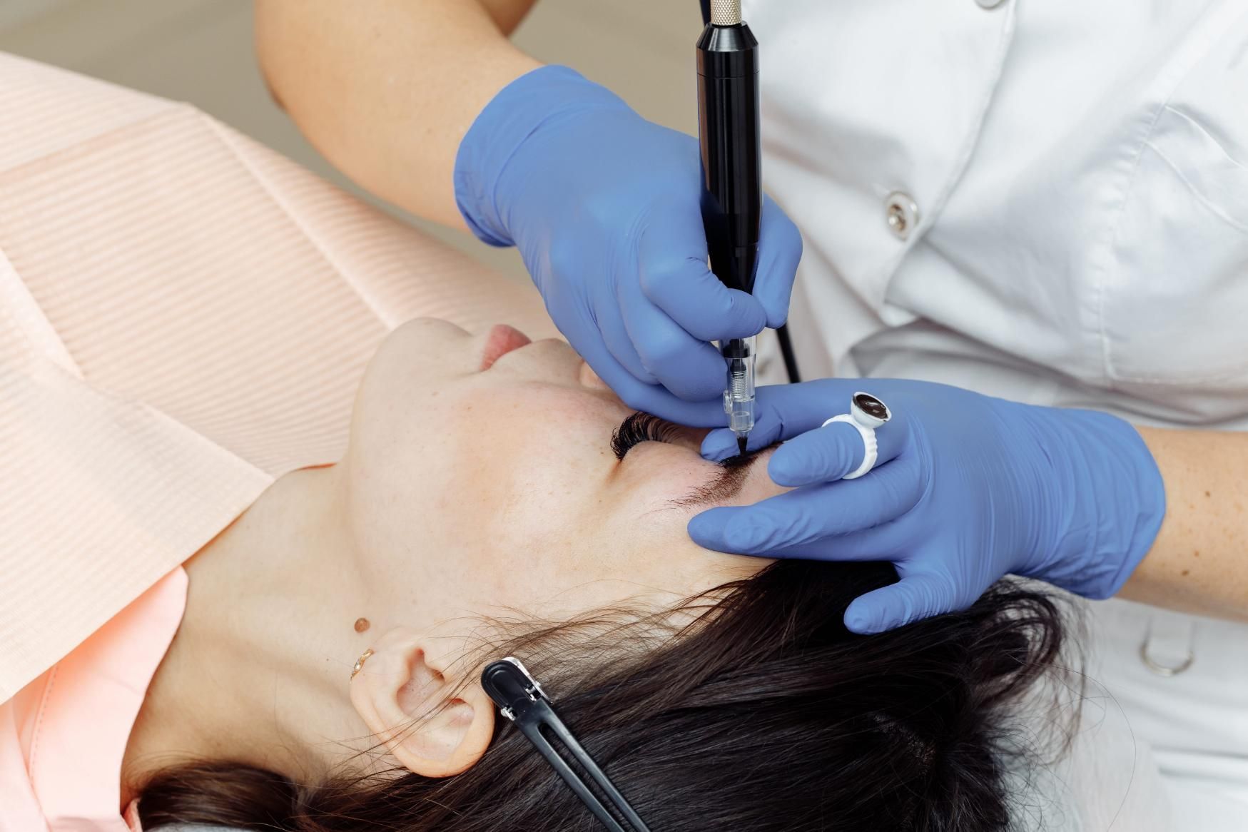 Procedimiento cosmético en el rostro de una clienta con un dispositivo de mano y guantes.