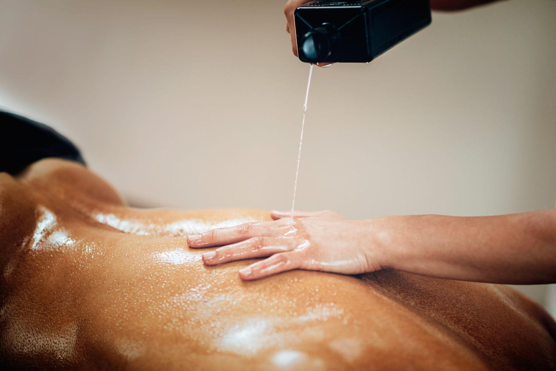Masajista vertiendo aceite en la espalda de un cliente durante un tratamiento de spa.