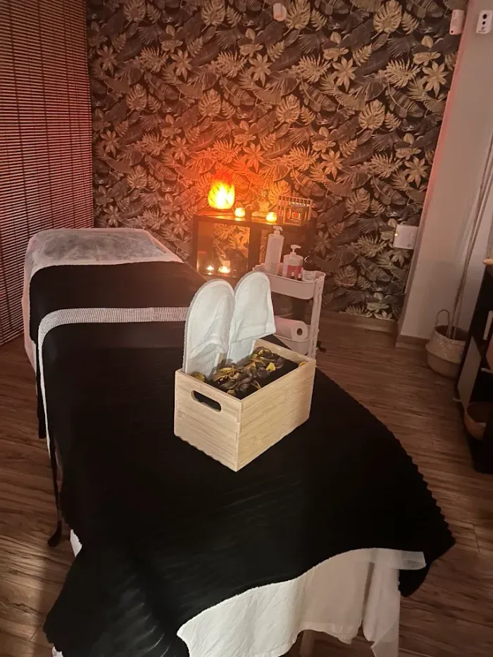 Camilla de masaje con toallas blancas dobladas y una sala de spa iluminada con velas, con papel pintado floral y luz cálida.