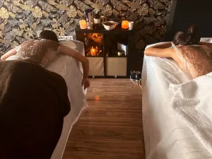 Dos personas tumbadas boca abajo sobre camillas de masaje en una sala de spa con poca luz
