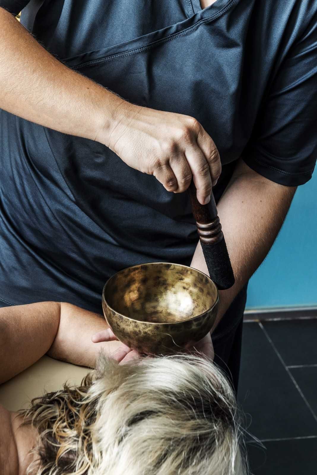 Persona que utiliza un mazo para golpear un cuenco cantor sobre la cabeza de una persona, posiblemente durante una sesión de curación sonora.