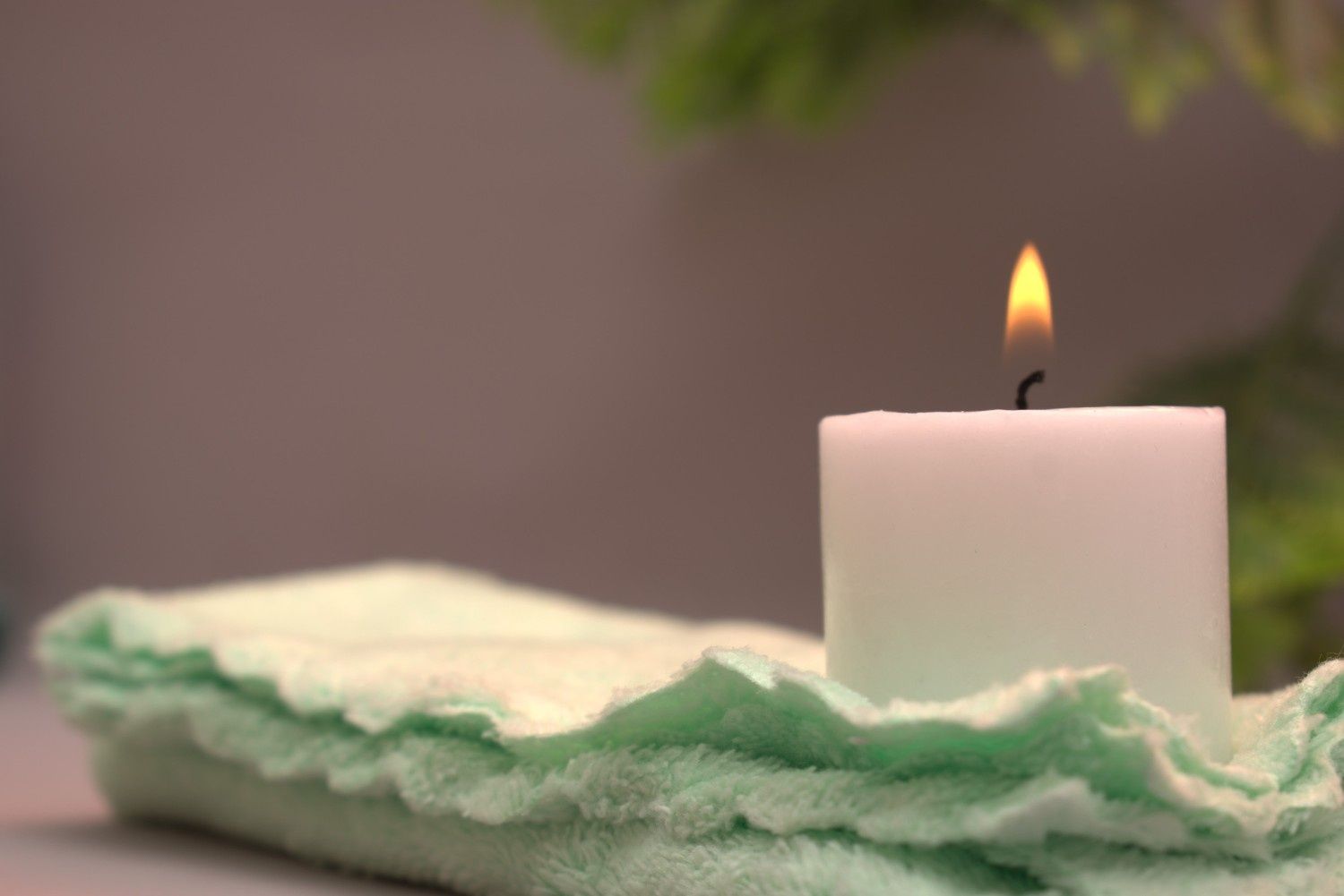 Vela blanca con llama encendida sobre una superficie de fieltro de color verde claro; fondo borroso.