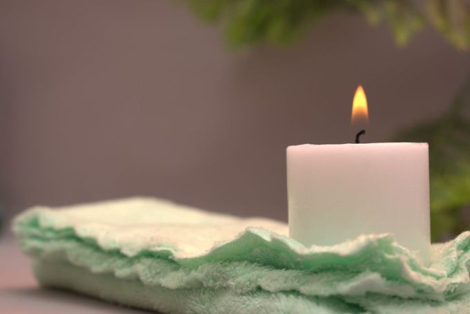 Vela blanca con llama encendida sobre una superficie de fieltro de color verde claro; fondo borroso.