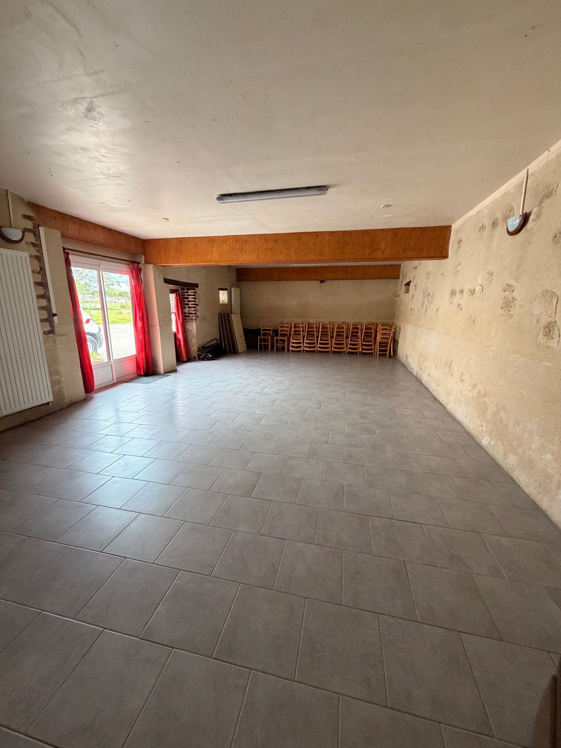 Pièce carrelée vide, murs blancs, plafond apparent et porte vitrée à cadre rouge sur la gauche.
