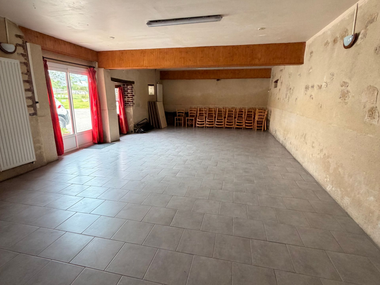 Pièce carrelée vide avec portes rouges, murs blancs et chaises empilées le long du mur du fond.