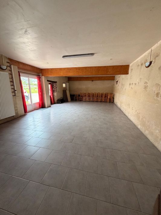 Longue salle à manger rustique avec poutres apparentes, sol carrelé et table dressée avec des chaises.
