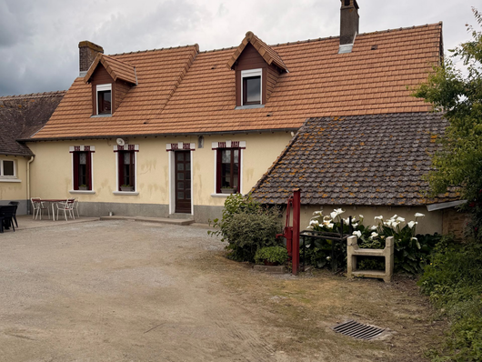 Maison rustique couleur crème avec toit de tuiles rouges et petit jardin dans une cour de village.