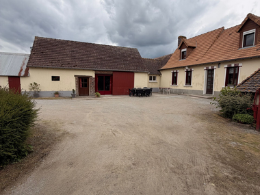 Cour intérieure avec sol en gravier, bâtiments beiges, portes rouges et ciel nuageux.