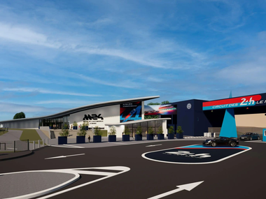 Vue extérieure d'une arène moderne avec une signalétique bleue et rouge, vue depuis un parking sous un ciel dégagé.