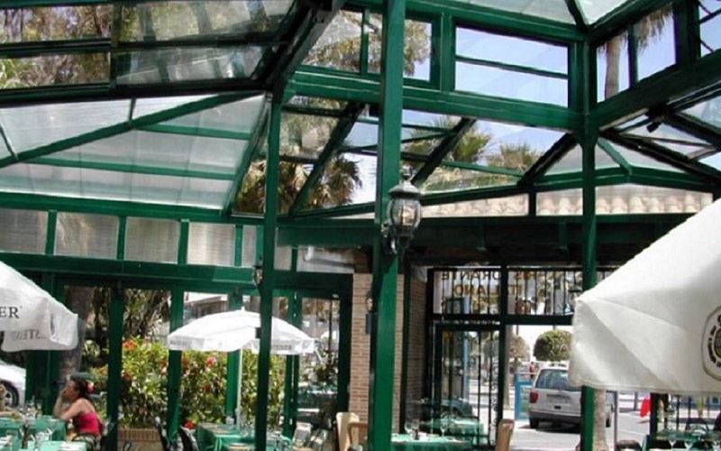 Un restaurante con mesas verdes y sombrillas blancas.