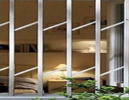 Un dormitorio con cama, mesitas de noche, lámparas y una ventana con reja de acero inoxidable.