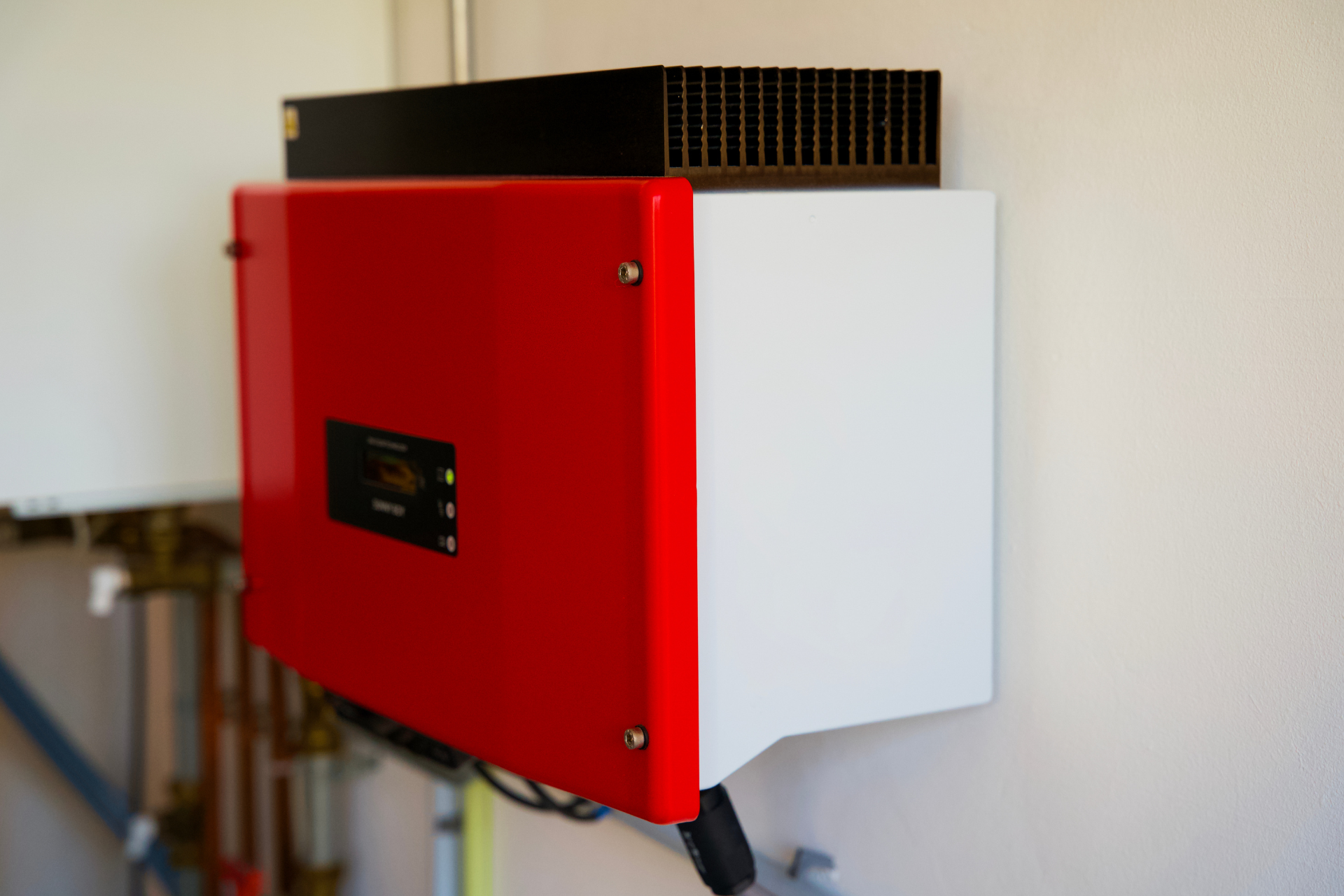 Boîtier d'onduleur solaire rouge et blanc monté sur un mur blanc. Dissipateur thermique noir sur le dessus.