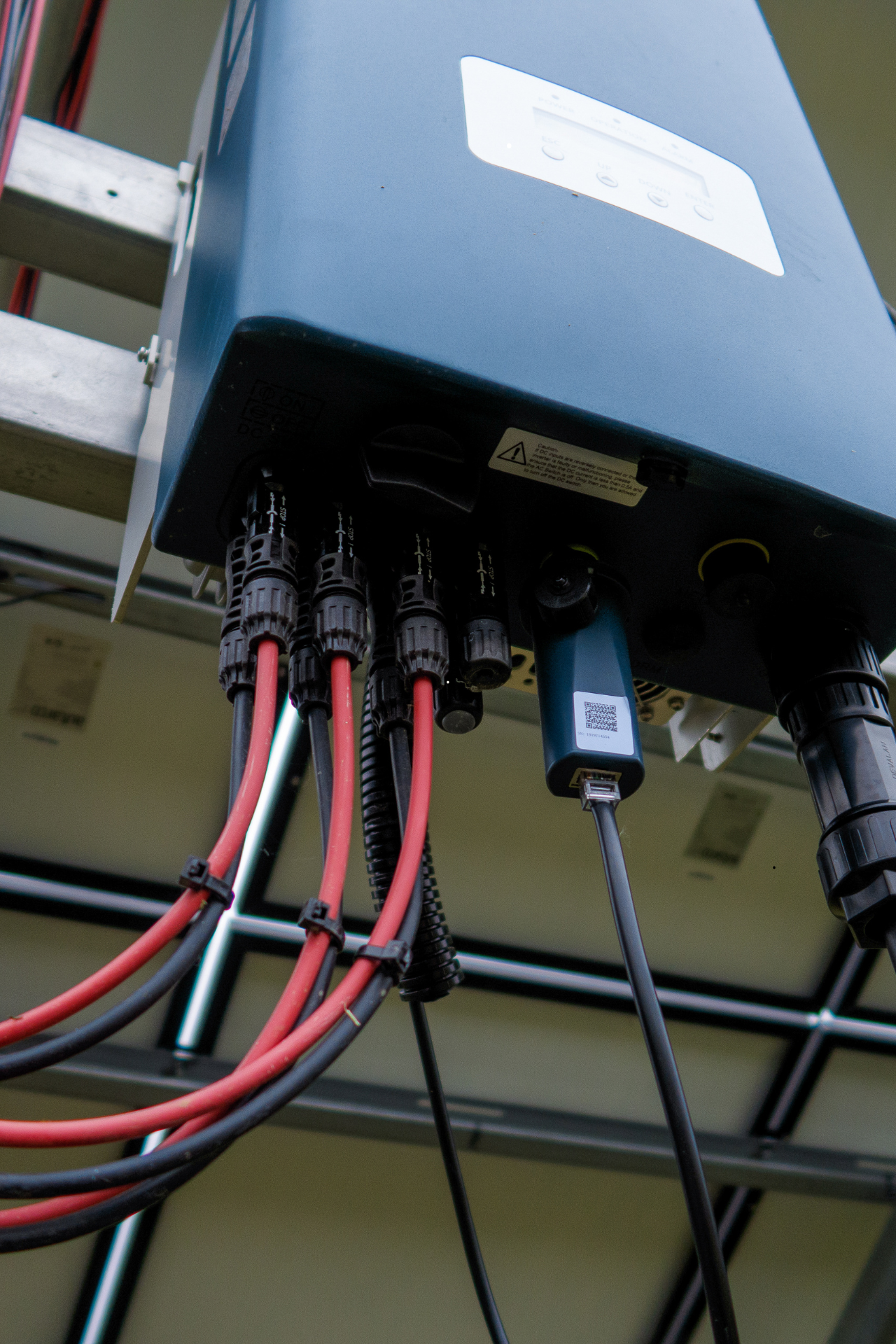 Onduleur de panneau solaire avec fils rouges et noirs, fixé sur un cadre métallique.