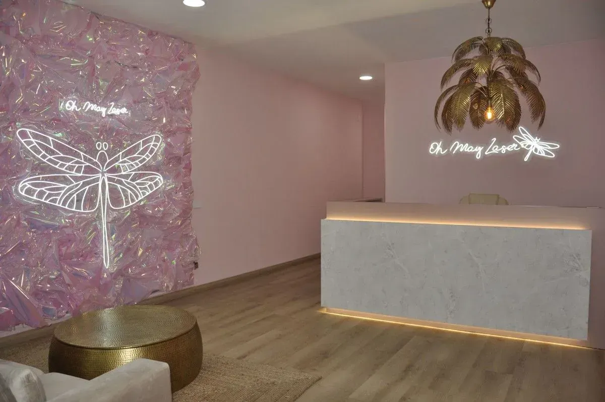 Área de recepción de color rosa con decoración de pared de libélula, detalles dorados y un mostrador de recepción.