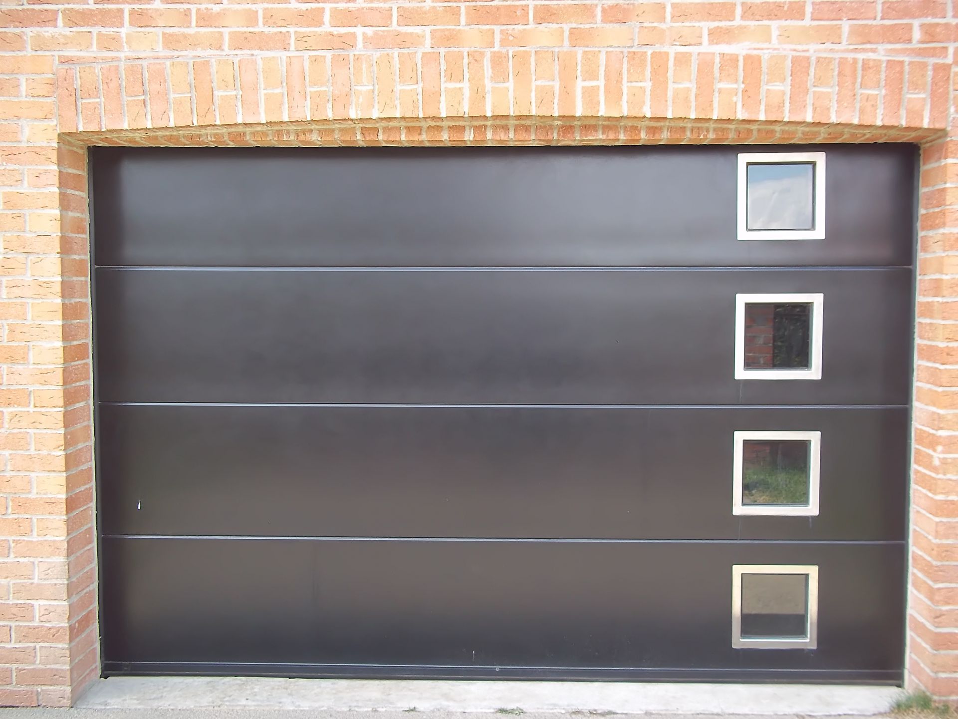 Porte de garage grise sur un bâtiment beige avec toit en tuiles de terre cuite, allée en gravier et clôture en bambou.