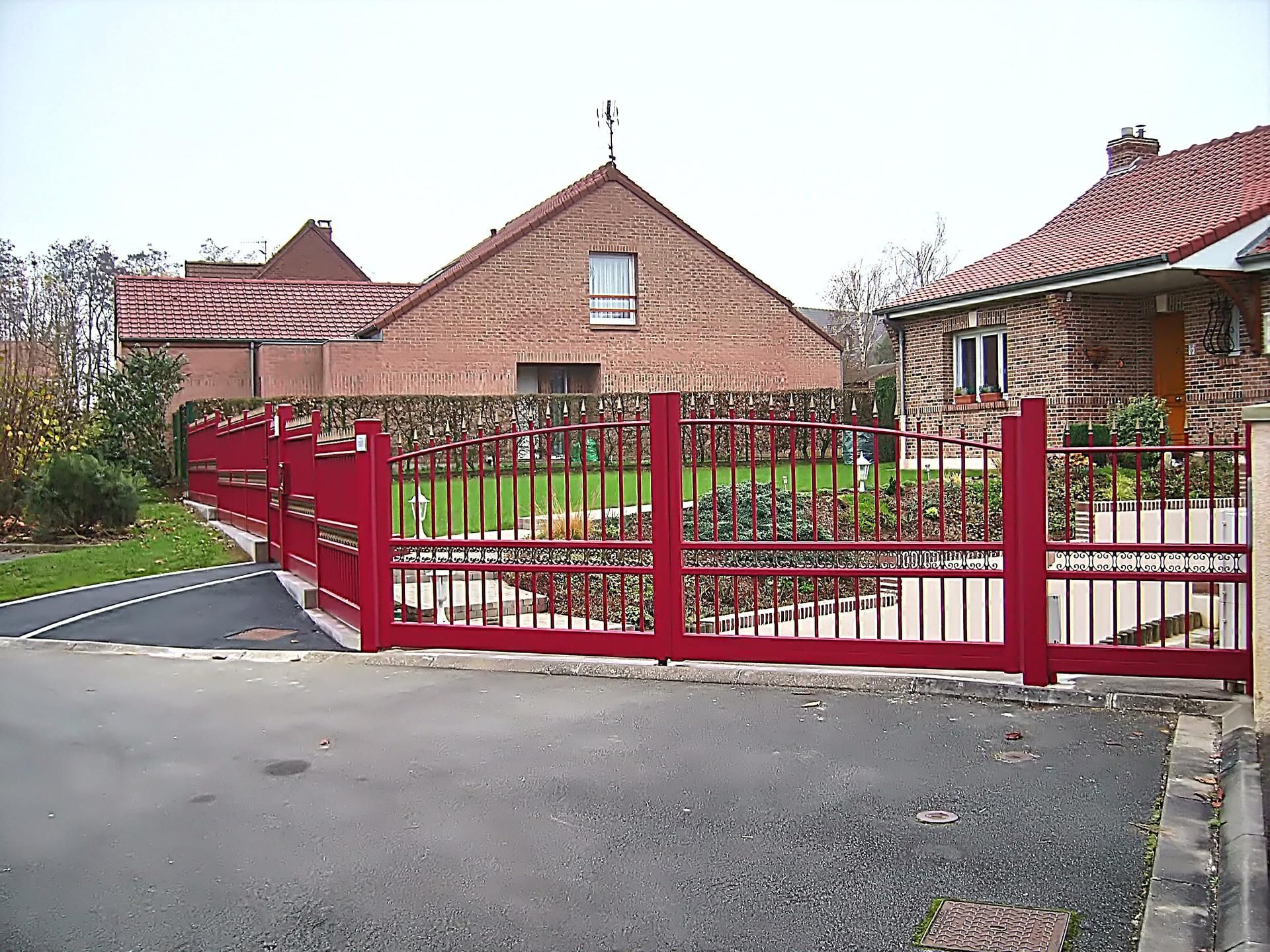 Une clôture métallique rouge entoure une cour avec une maison en briques et une allée pavée.