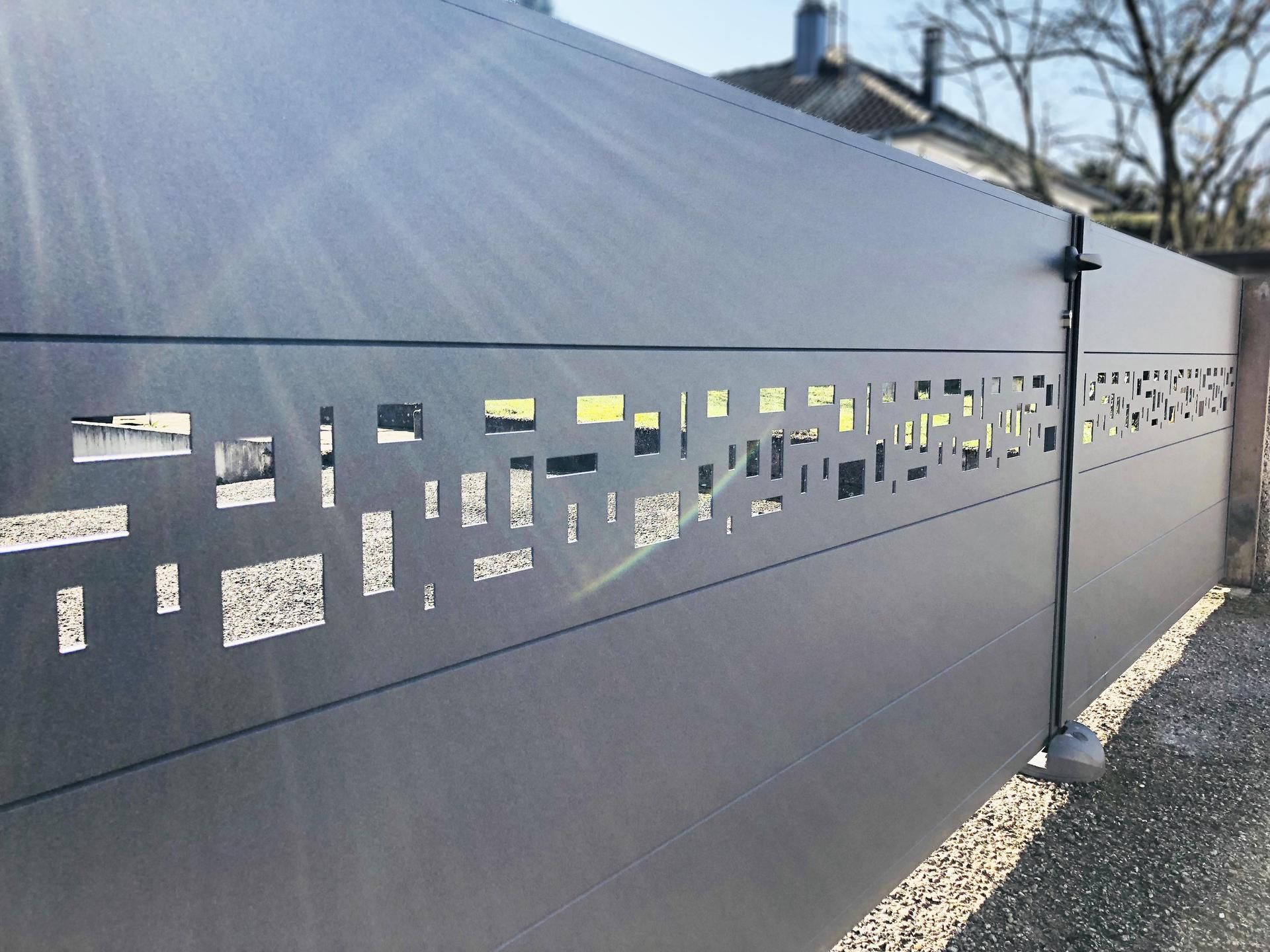 Clôture extérieure en métal gris foncé avec découpes géométriques.