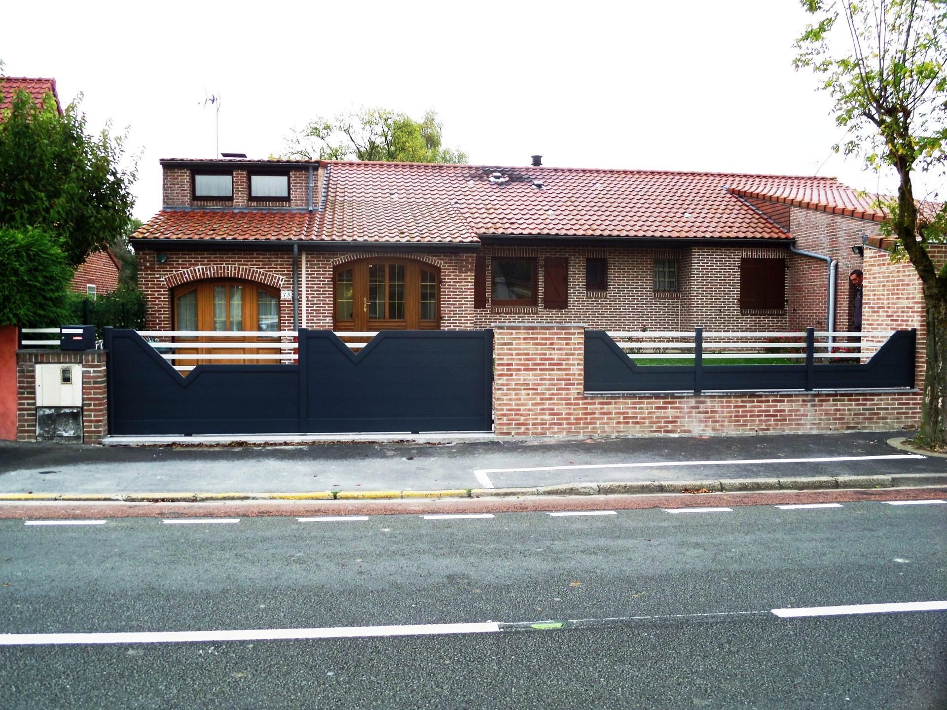 Maison en briques avec portail et clôture sombres, en bordure de rue.