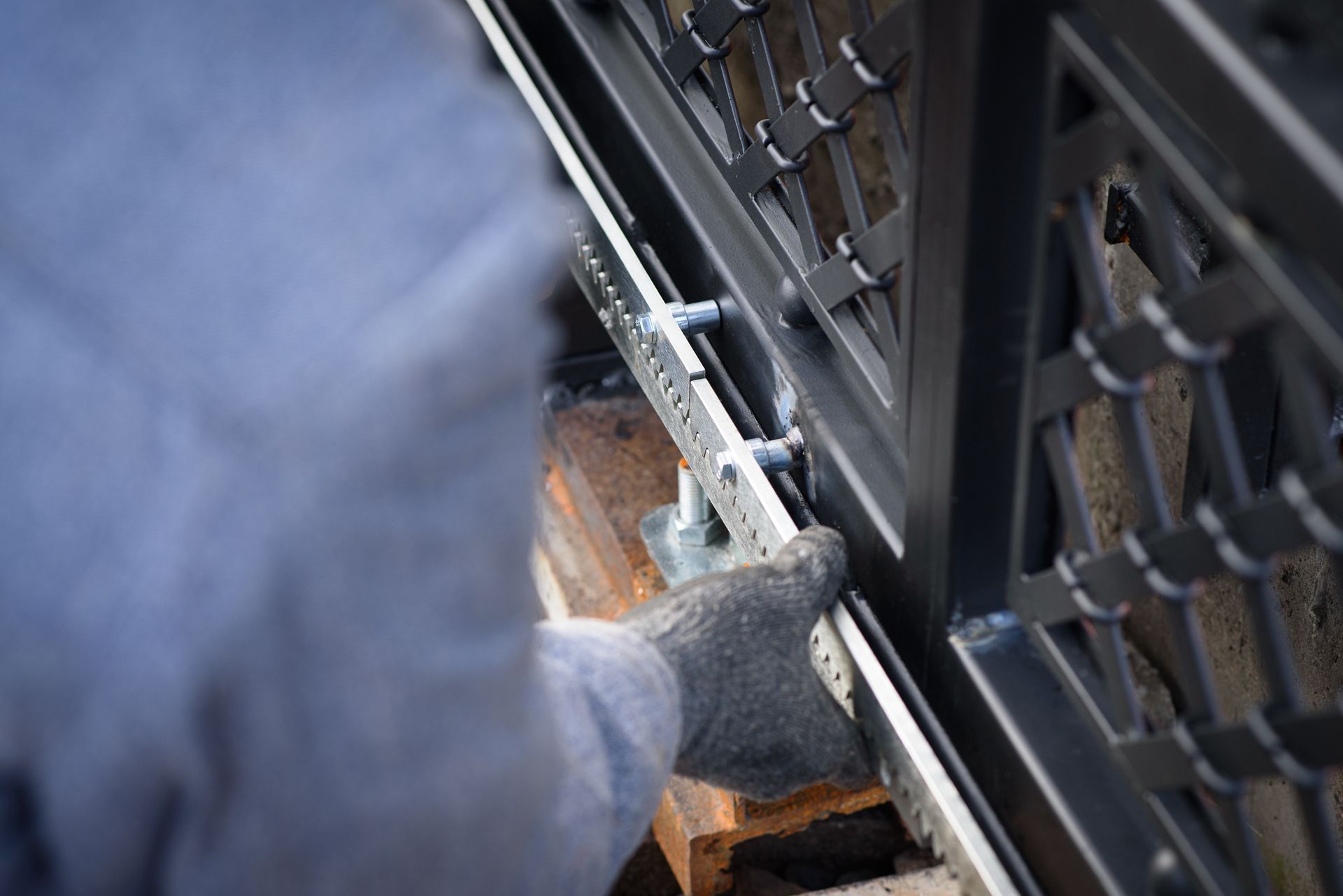 Une personne en tenue de protection installe un portail métallique avec des boulons.