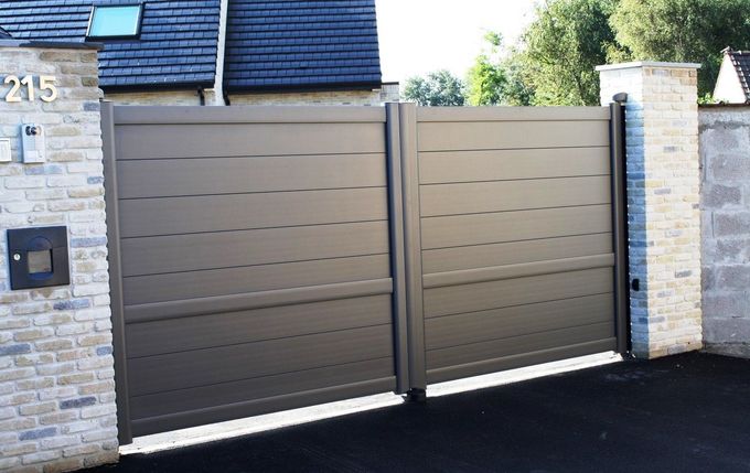 Portail coulissant en métal gris devant un bâtiment en briques.