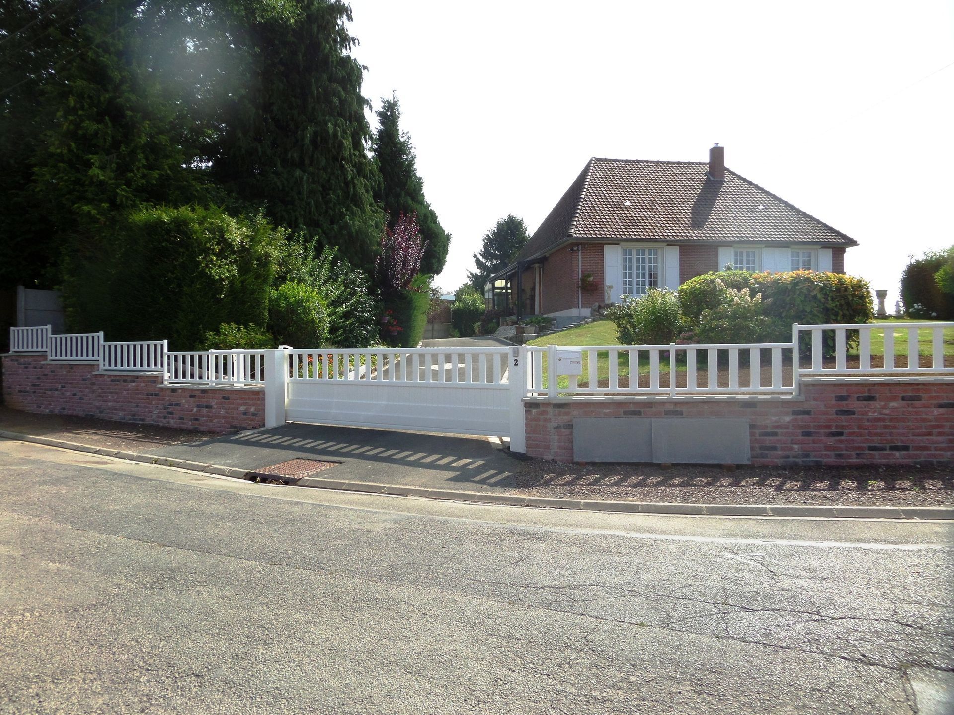 Portail et clôture en métal gris devant une maison. Un arbre est visible en arrière-plan.