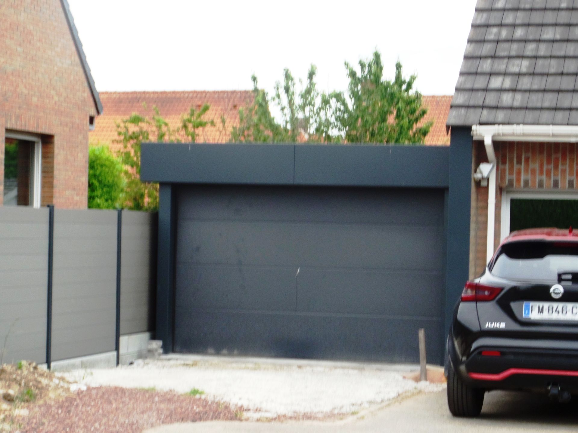 Extérieur de maison moderne avec porte de garage grise, murs blancs et allée en pierre.