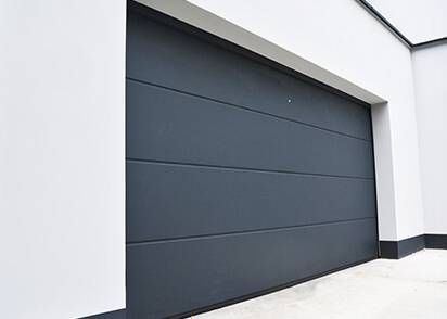 Porte de garage à panneaux horizontaux gris sur un bâtiment blanc.