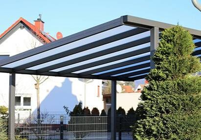 Un abri de voiture gris avec un toit translucide à rayures, devant une maison.