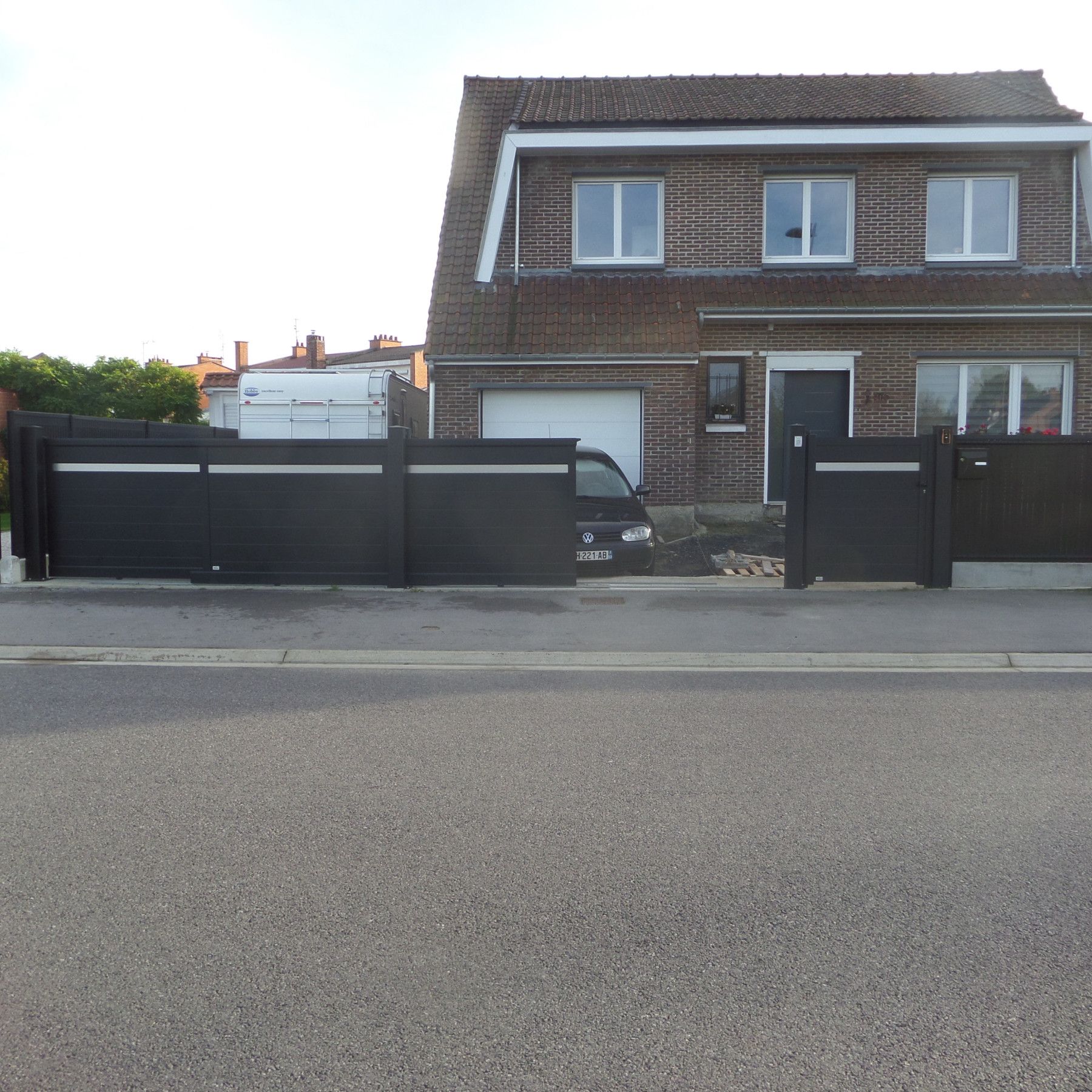Portail et clôture noirs devant une maison en briques, avec une camionnette garée derrière.