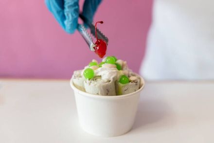 Una mano con guante añade un sirope rojo a una copa de helado de vainilla con cerezas verdes