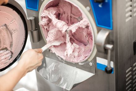 Mano sacando helado rosa de una máquina de acero inoxidable con una espátula