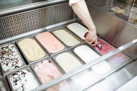 Una mano alcanza una vitrina de helados con una variedad de sabores en bandejas