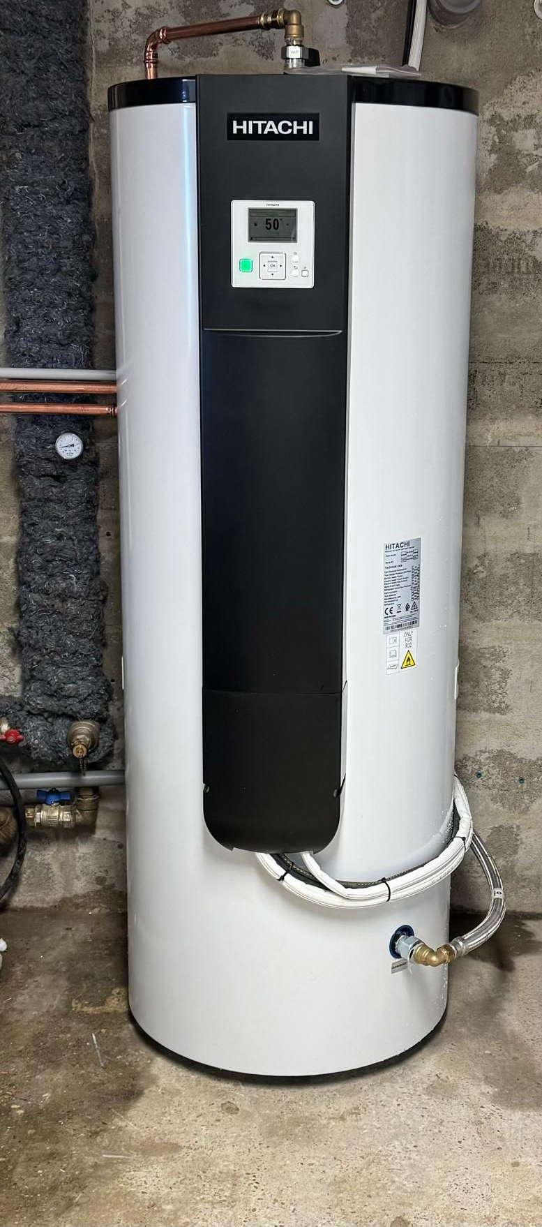 Chauffe-eau blanc et noir contre un mur en béton gris.