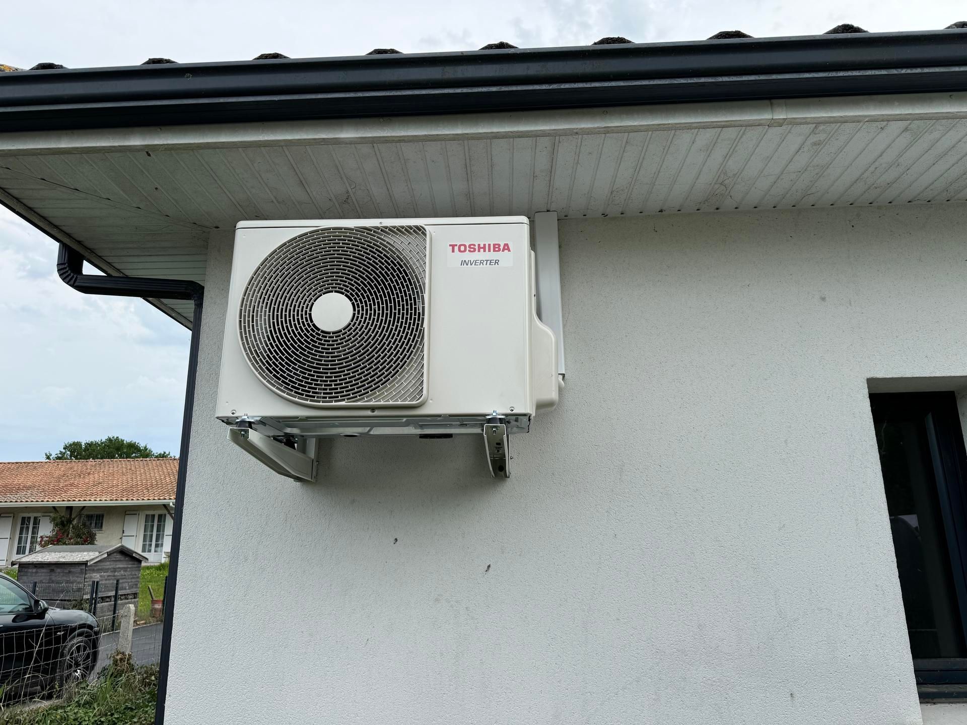 Unité de climatisation blanche fixée sur un mur extérieur blanc, à côté d'une fenêtre.