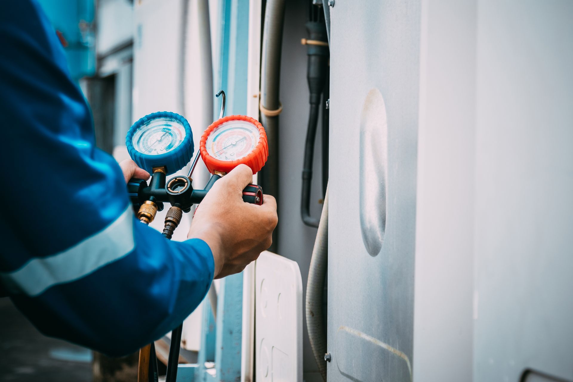 Technicien utilisant des manomètres sur un climatiseur, en extérieur, gros plan sur ses mains.