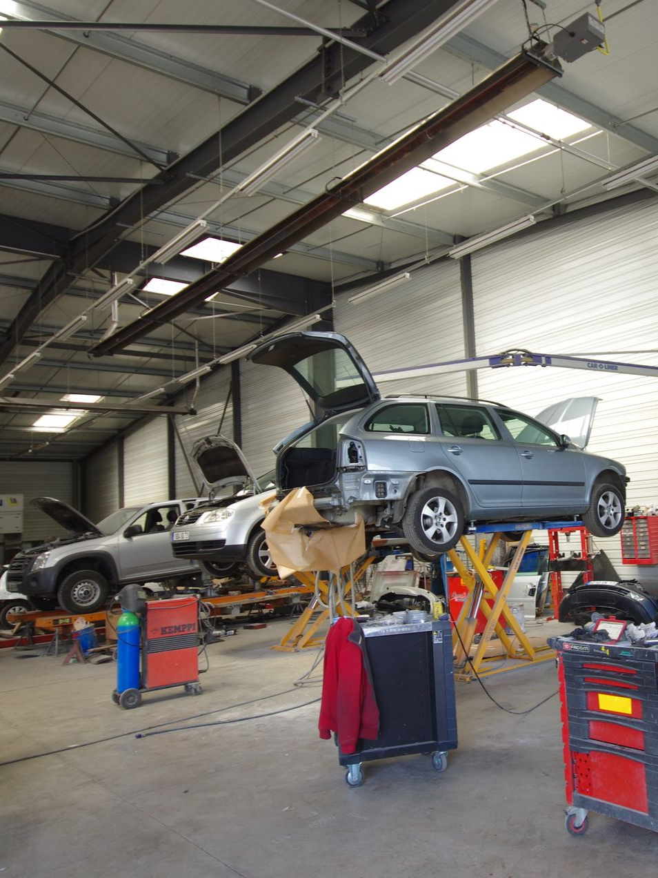 Deux voitures grises en réparation dans un atelier automobile équipé de ponts élévateurs.