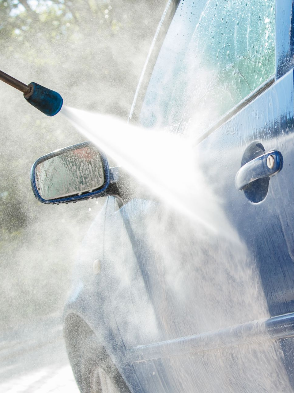 Un nettoyeur haute pression lave le côté et le rétroviseur d'une voiture bleue.