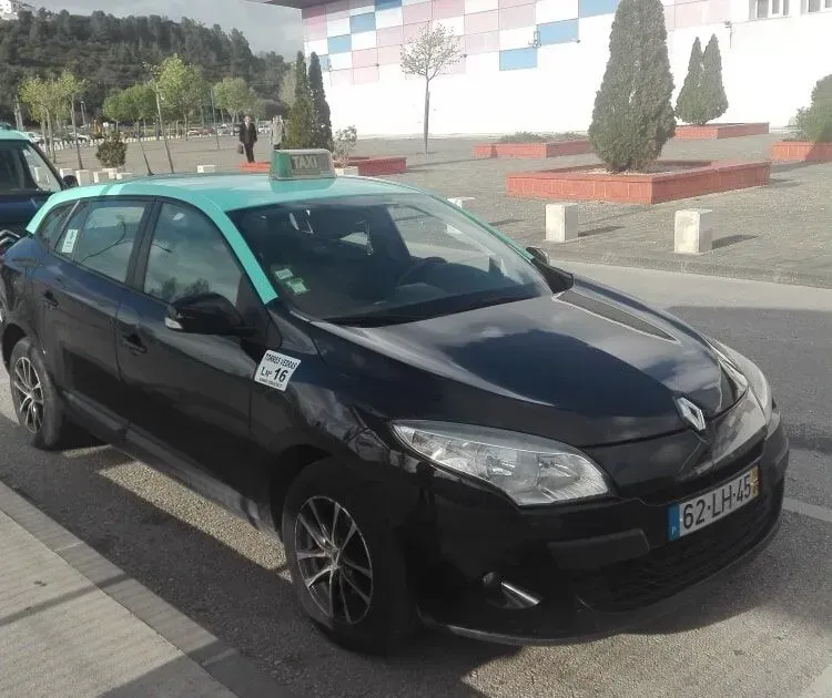 Táxi Renault preto com teto verde estacionado em frente a um prédio.
