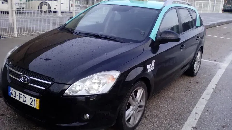 Uma Kia Ceed station wagon preta com teto azul, estacionada em um estacionamento, possivelmente um táxi.