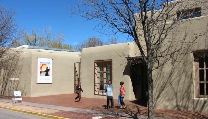 Adobe-style building with figures in front; poster on wall, sunny day.