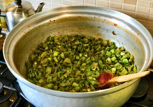 Large pot of chopped green beans simmering on a stovetop, with a wooden spoon inside.