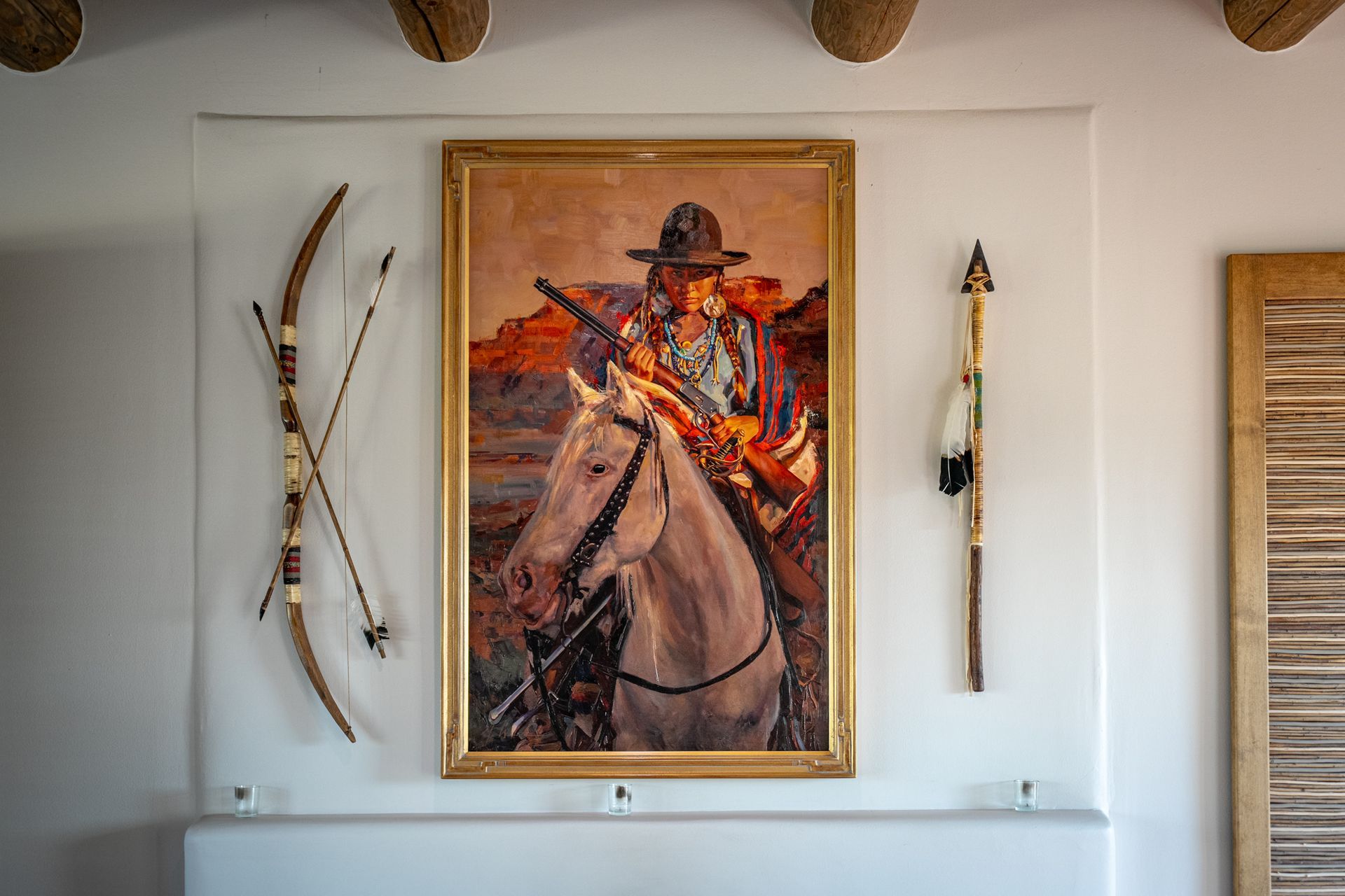 Painting of Native American on horseback, with a bow and arrow, and staff on a white wall.