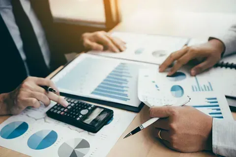 Dos hombres están sentados en una mesa mirando gráficos y una calculadora.