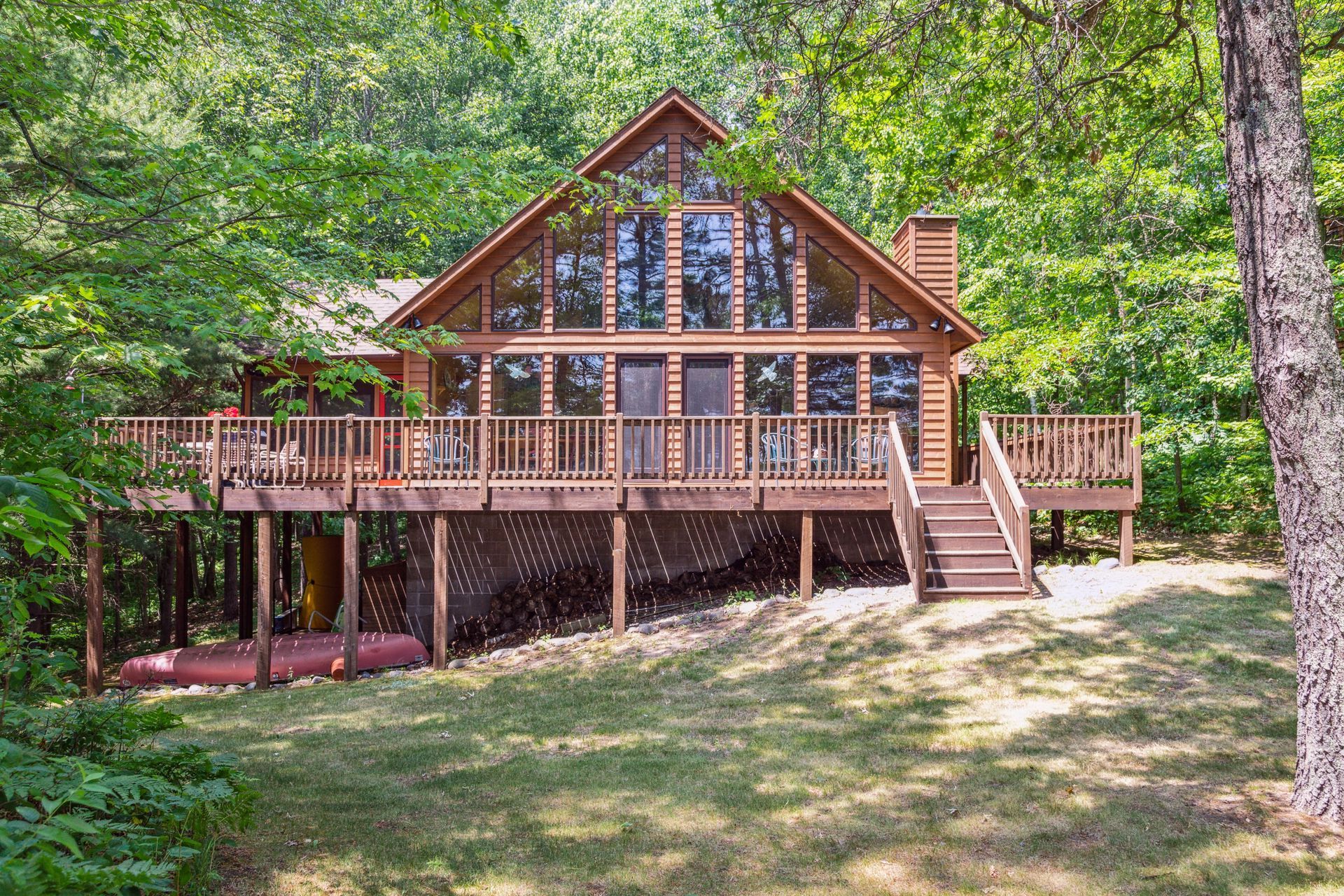 A large log cabin with a large deck in the middle of a forest.