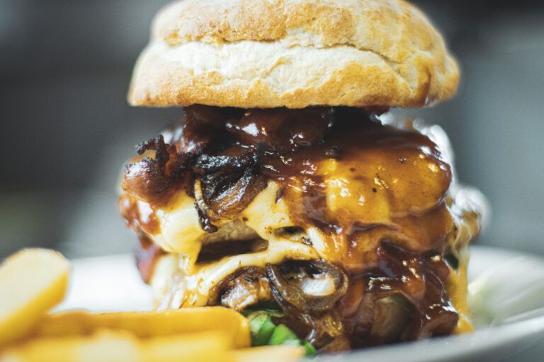 Nahaufnahme eines Cheeseburgers mit geschmolzenem Käse, karamellisierten Zwiebeln und Pommes frites auf einem Teller