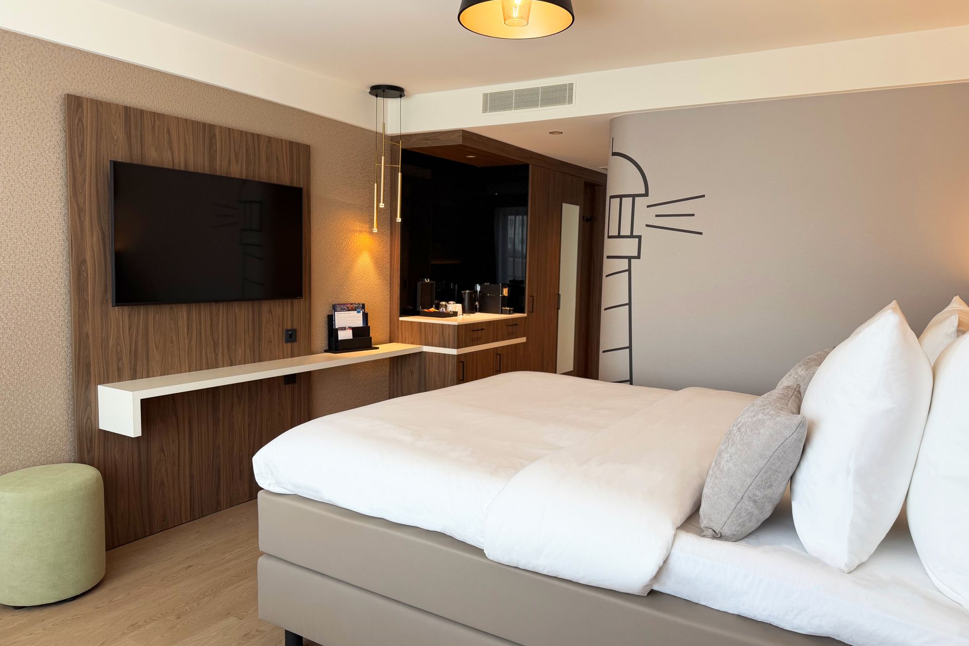 Moderne hotelkamer met een bed, aan de muur gemonteerde tv, kaptafel en groot raam.