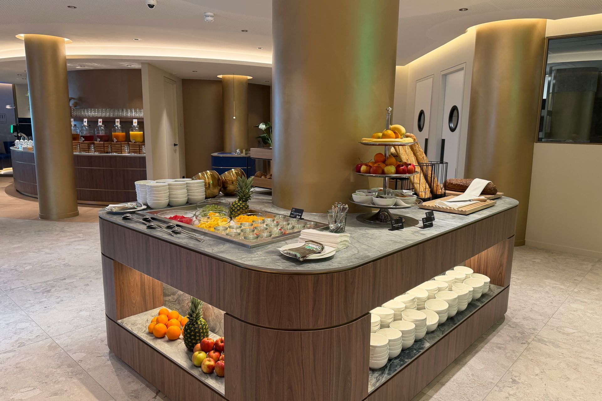 Buffettafel met schalen vol gebak en donuts onder een turquoise neonbord in een eetkamer.