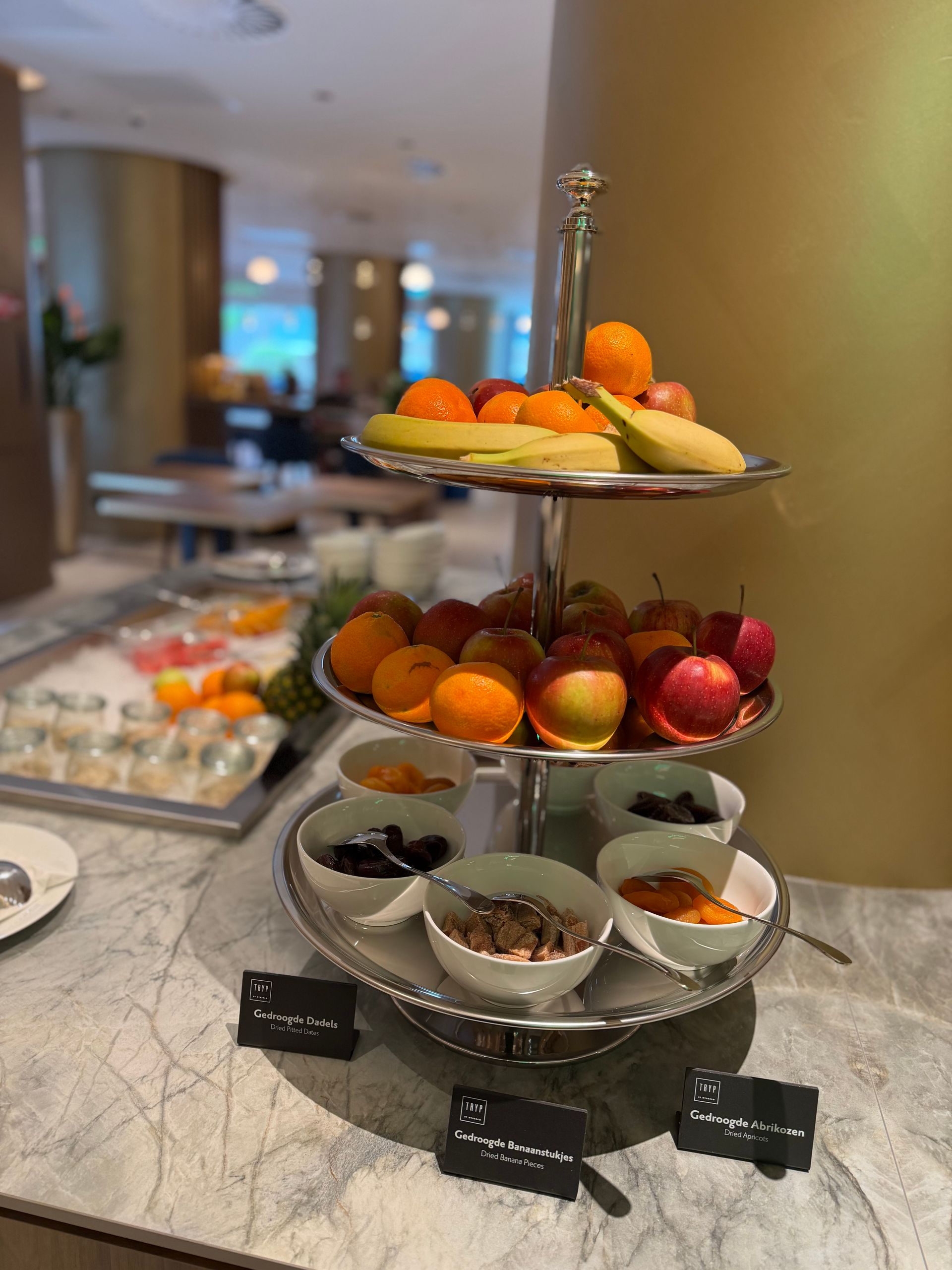 Een drielaags buffet met fruit en yoghurt op een marmeren toonbank in een restaurantgedeelte van een hotel.