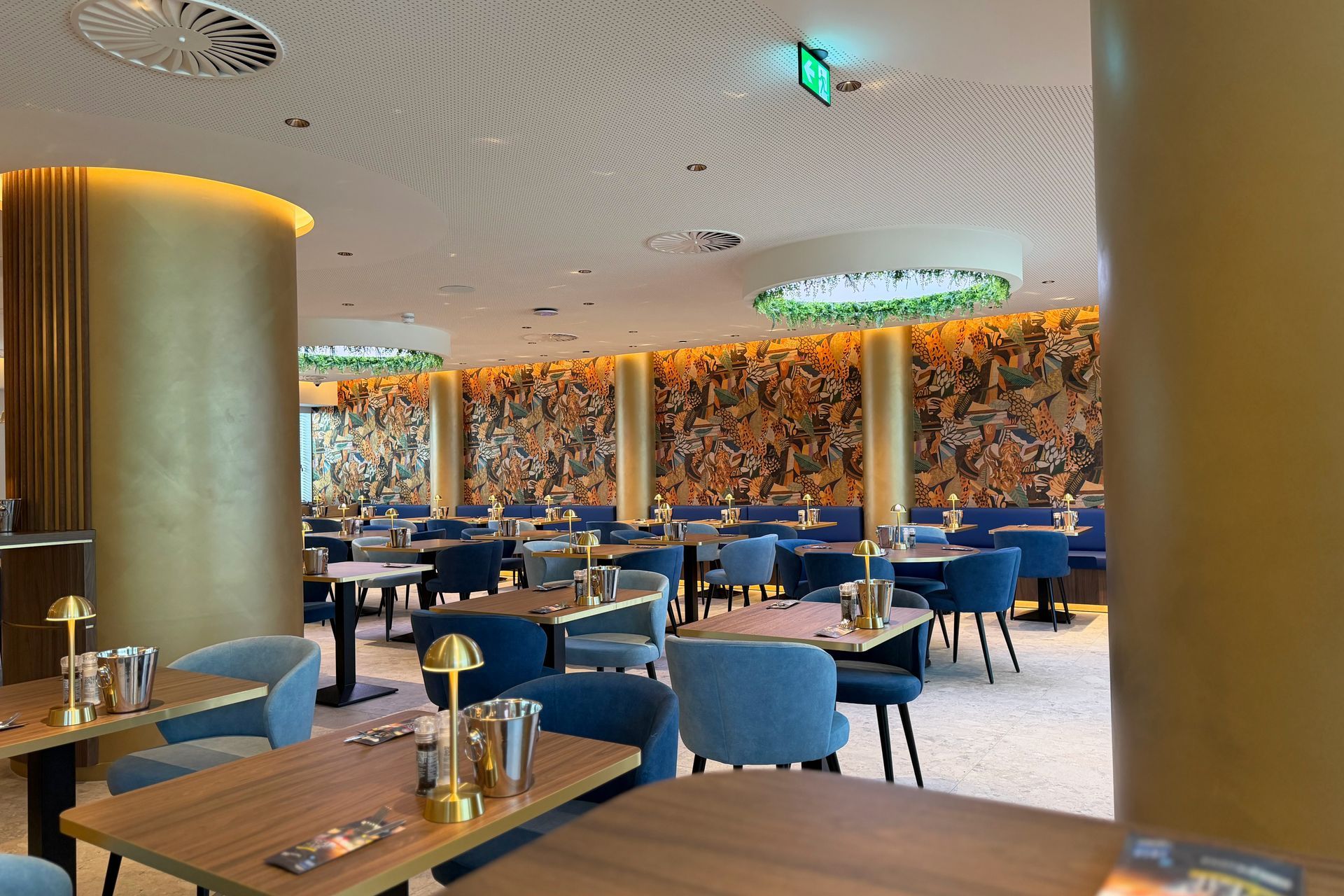 Lege, moderne restaurantzaal met blauwe stoelen, houten tafels en mozaïekwanddecoratie.